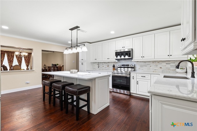 kitchen with sink, a kitchen island, white cabinetry, appliances with stainless steel finishes, and decorative light fixtures