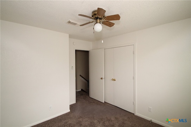 unfurnished bedroom with a textured ceiling, a closet, dark carpet, and ceiling fan