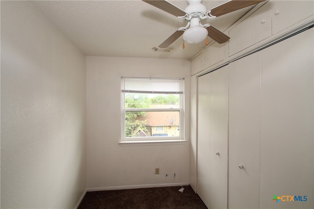 unfurnished bedroom with dark colored carpet, a textured ceiling, a closet, and ceiling fan