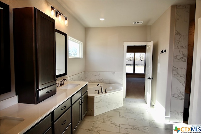 bathroom with vanity, a relaxing tiled tub, and a healthy amount of sunlight