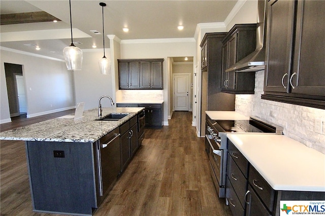 kitchen featuring stainless steel appliances, hanging light fixtures, sink, wall chimney exhaust hood, and a kitchen island with sink