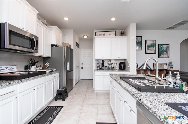 kitchen with appliances with stainless steel finishes, white cabinetry, light stone counters, and sink