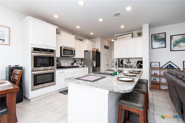 kitchen featuring a breakfast bar, stainless steel appliances, white cabinets, and an island with sink