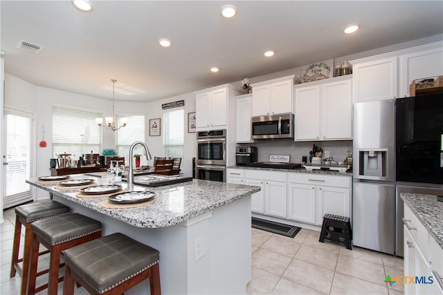 kitchen with stainless steel appliances, an inviting chandelier, white cabinets, and an island with sink