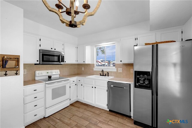 kitchen featuring decorative backsplash, sink, white cabinetry, appliances with stainless steel finishes, and decorative light fixtures