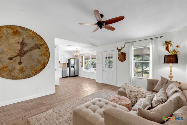 living room featuring ceiling fan with notable chandelier, light wood-type flooring, and vaulted ceiling