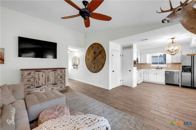 living room featuring ceiling fan with notable chandelier, sink, light wood-type flooring, and vaulted ceiling