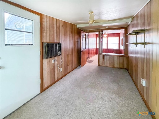unfurnished living room featuring wood walls, light carpet, and a ceiling fan