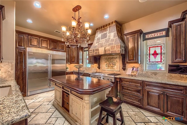 kitchen featuring stone tile floors, visible vents, a center island, stainless steel built in refrigerator, and custom range hood