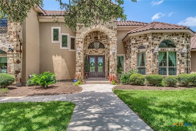 doorway to property featuring french doors, a yard, stucco siding, stone siding, and a tiled roof