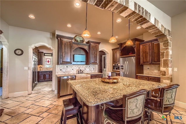 kitchen featuring arched walkways, a kitchen island, appliances with stainless steel finishes, decorative light fixtures, and dark brown cabinets