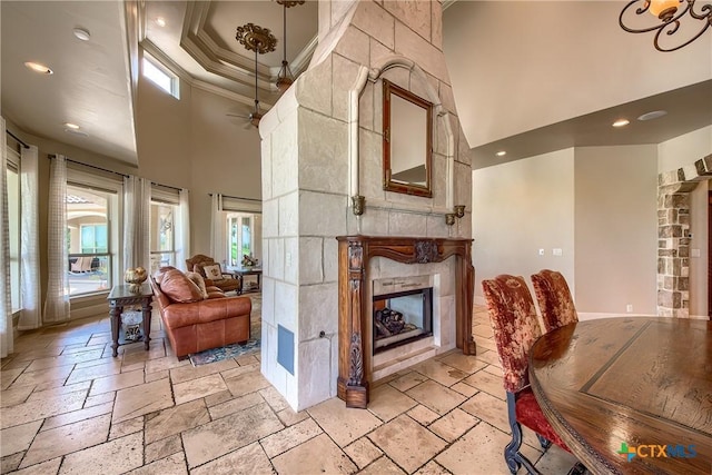 living room featuring a fireplace, a high ceiling, crown molding, and stone tile floors