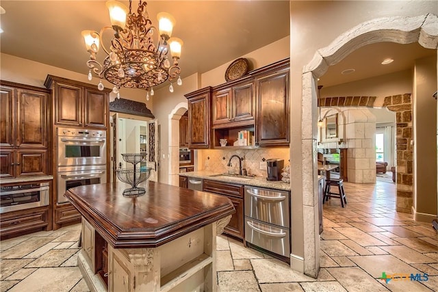 kitchen with arched walkways, stainless steel double oven, open shelves, stone tile flooring, and pendant lighting