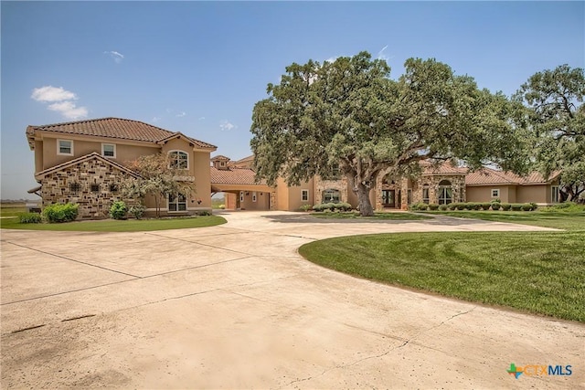 mediterranean / spanish house with curved driveway, a tiled roof, a front lawn, and stucco siding