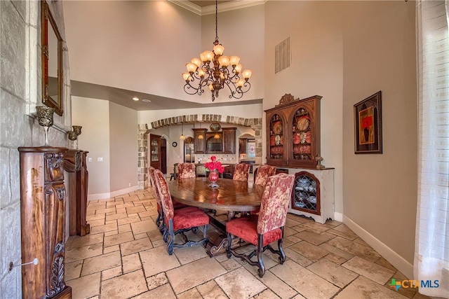 dining room featuring baseboards, arched walkways, a high ceiling, stone tile flooring, and a notable chandelier