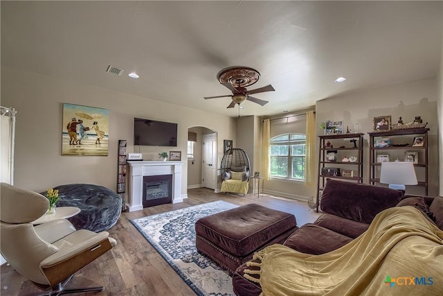 living room featuring baseboards, arched walkways, ceiling fan, wood finished floors, and a fireplace