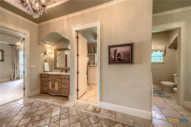 bathroom featuring stone tile floors, toilet, ornamental molding, vanity, and a notable chandelier