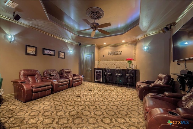 cinema featuring a tray ceiling, light colored carpet, visible vents, ornamental molding, and a ceiling fan