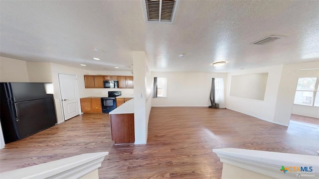 kitchen with a textured ceiling, hardwood / wood-style flooring, and black appliances