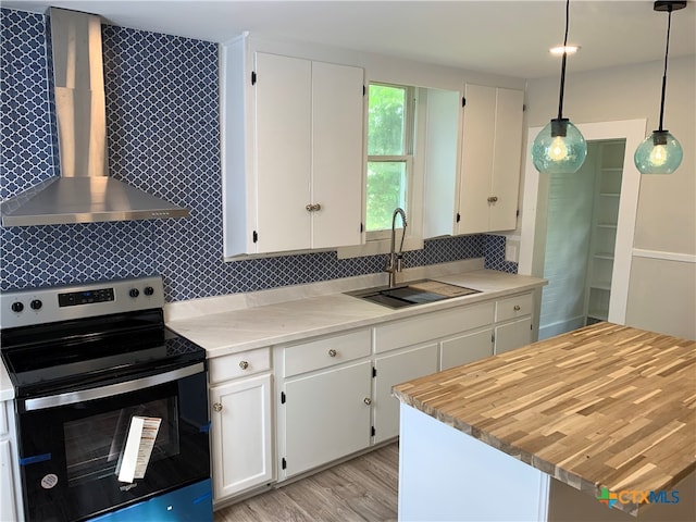 kitchen with stainless steel range with electric cooktop, wall chimney range hood, decorative light fixtures, sink, and white cabinets