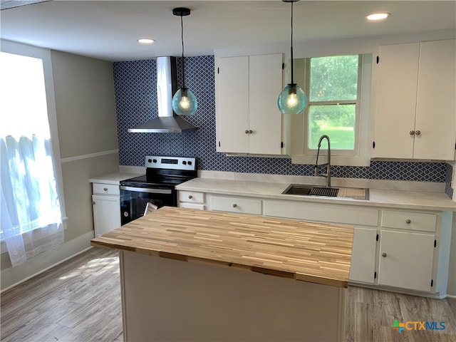 kitchen featuring wall chimney range hood, white cabinetry, decorative light fixtures, sink, and stainless steel electric stove