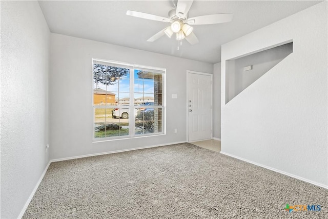 carpeted spare room with ceiling fan, a textured wall, and baseboards