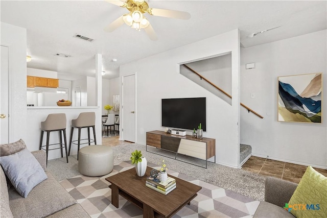 living room featuring a ceiling fan, visible vents, stairway, and tile patterned floors