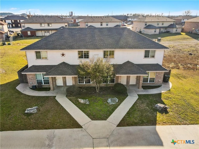 view of front of house featuring roof with shingles, a residential view, a front lawn, and brick siding