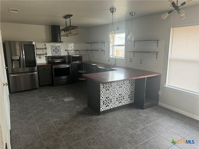 kitchen featuring pendant lighting, wall chimney range hood, stainless steel appliances, and kitchen peninsula