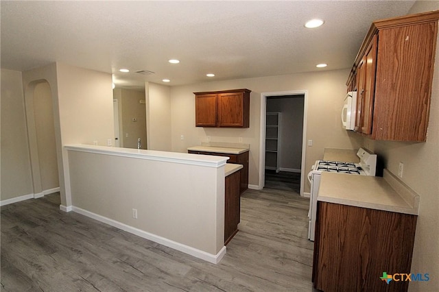 kitchen with light wood-type flooring, white appliances, a peninsula, brown cabinets, and recessed lighting