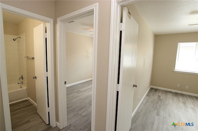 hall featuring a textured ceiling, baseboards, and wood finished floors