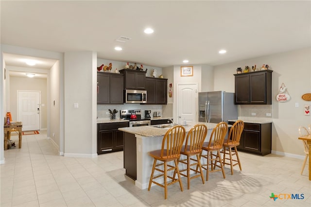 kitchen featuring backsplash, a breakfast bar area, an island with sink, dark brown cabinets, and stainless steel appliances