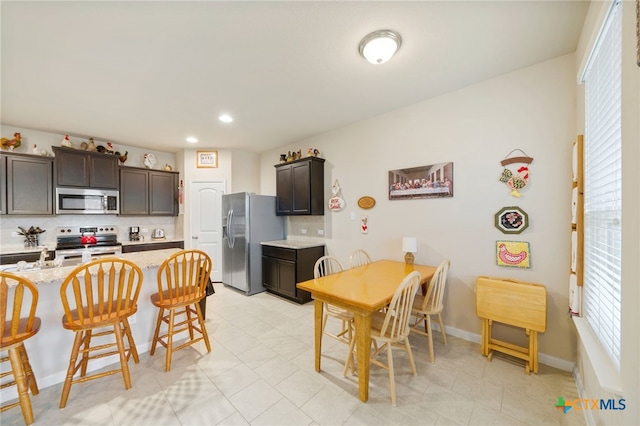 kitchen with tasteful backsplash, dark brown cabinetry, light stone counters, and appliances with stainless steel finishes