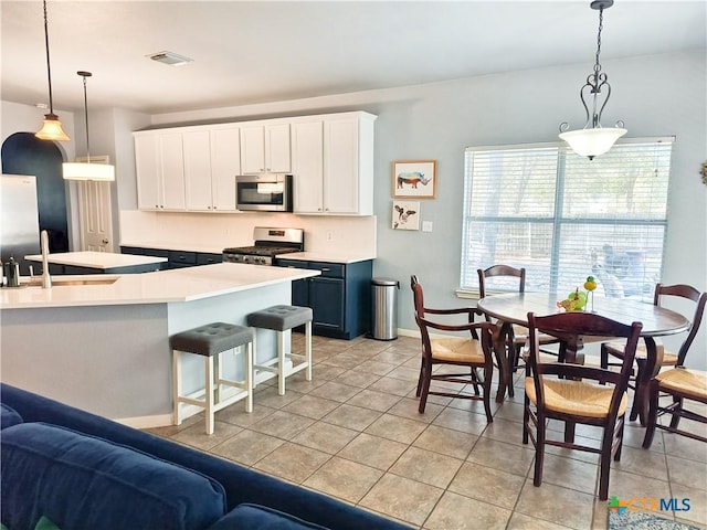 kitchen featuring appliances with stainless steel finishes, decorative light fixtures, white cabinetry, and a breakfast bar area