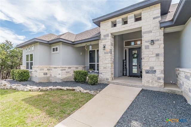 doorway to property featuring stone siding, a shingled roof, and stucco siding