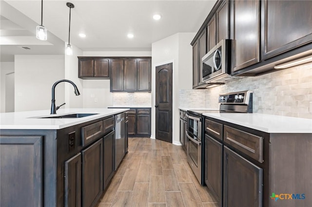 kitchen with sink, dark brown cabinets, stainless steel appliances, a center island with sink, and decorative light fixtures