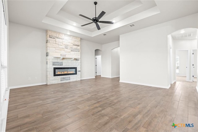 unfurnished living room featuring a raised ceiling, a fireplace, and ceiling fan