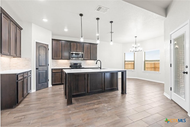 kitchen featuring sink, range with electric cooktop, dark brown cabinetry, an island with sink, and decorative light fixtures