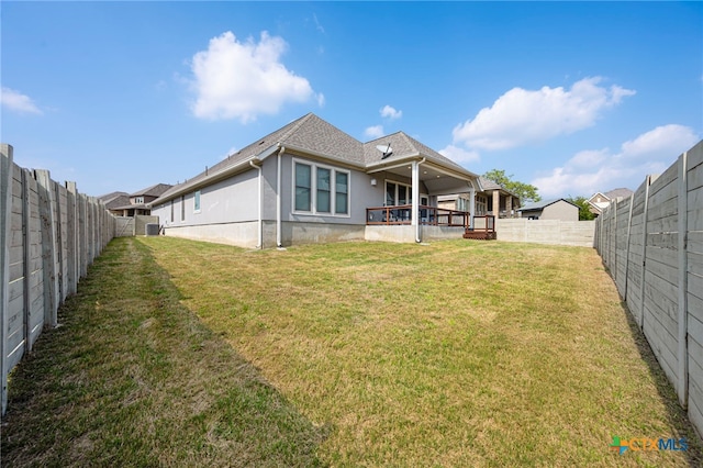 rear view of house with a fenced backyard, a lawn, and stucco siding