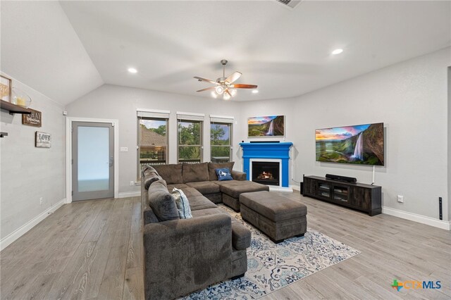 living area with baseboards, a lit fireplace, a ceiling fan, and light wood finished floors