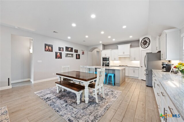 dining space with arched walkways, baseboards, light wood-style floors, and recessed lighting
