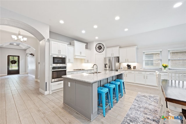 kitchen with decorative backsplash, a sink, arched walkways, light wood-style flooring, and appliances with stainless steel finishes