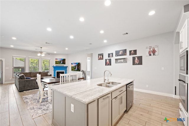kitchen featuring a sink, a fireplace, stainless steel appliances, a kitchen island with sink, and ceiling fan