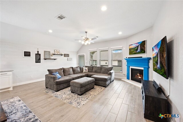 living room featuring light wood-style flooring, visible vents, baseboards, ceiling fan, and a glass covered fireplace