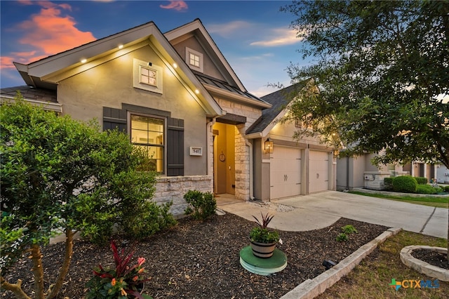 view of front facade featuring stone siding, driveway, stucco siding, and an attached garage