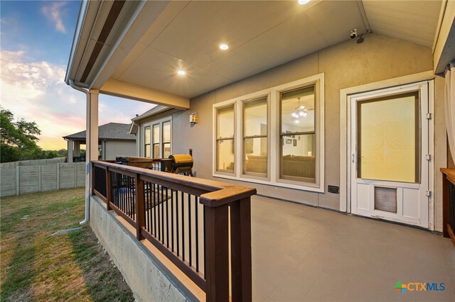 deck at dusk featuring grilling area, a lawn, fence, and a patio area
