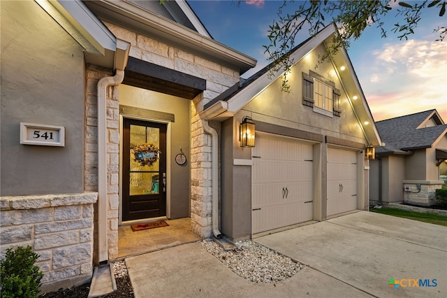 doorway to property featuring stone siding, concrete driveway, and a garage