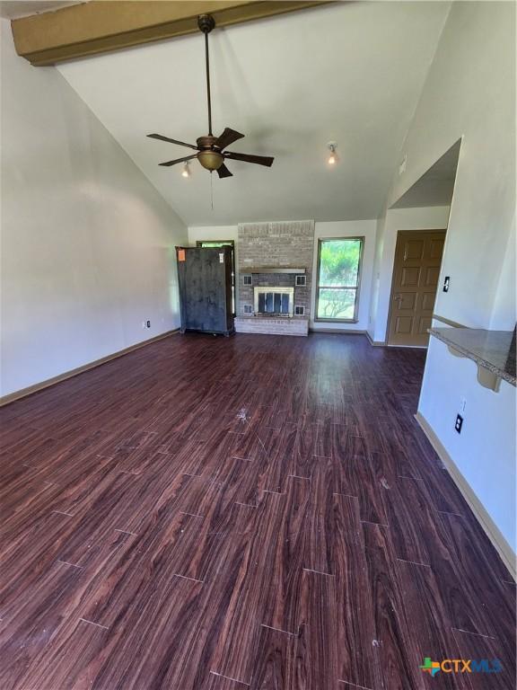 unfurnished living room with dark wood-type flooring, ceiling fan, high vaulted ceiling, a fireplace, and beamed ceiling