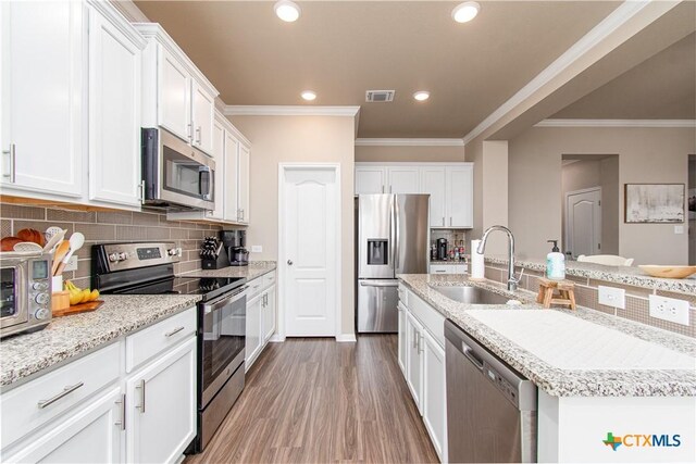 10207 Six Shooter Ln, Temple, TX 76502 - kitchen with appliances with stainless steel finishes, a sink, white cabinetry, light wood-style flooring, and crown molding