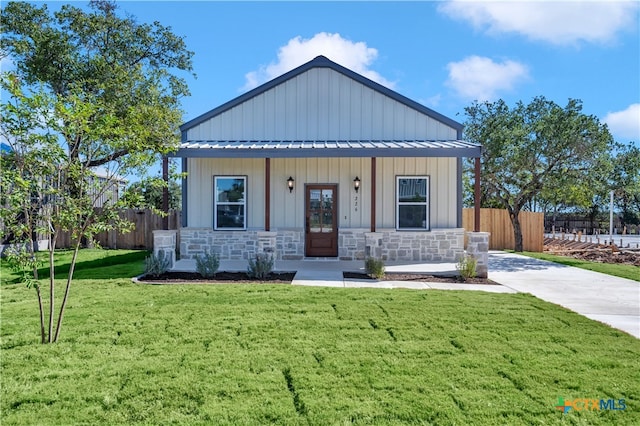 modern inspired farmhouse featuring a front yard, fence, stone siding, board and batten siding, and metal roof